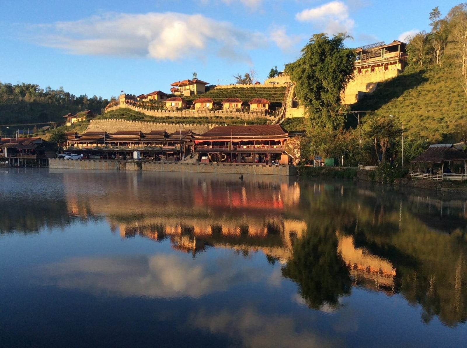 Lac de Mae Hong Son au coucher du soleil avec reflets dorés et village en bord d'eau entouré de montagnes