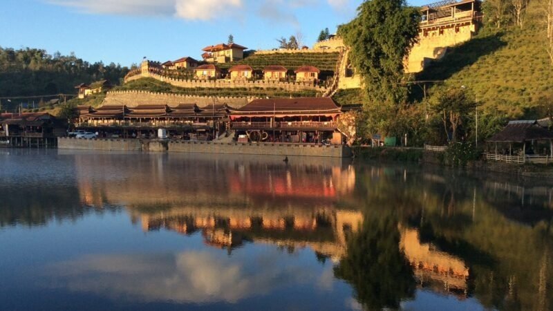 Lac de Mae Hong Son au coucher du soleil avec reflets dorés et village en bord d'eau entouré de montagnes