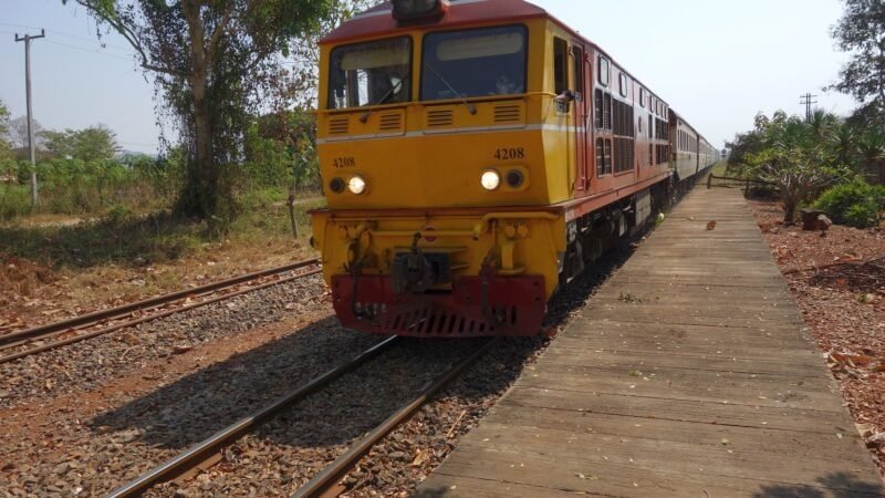 Train coloré en Thaïlande sur une voie ferrée rurale.