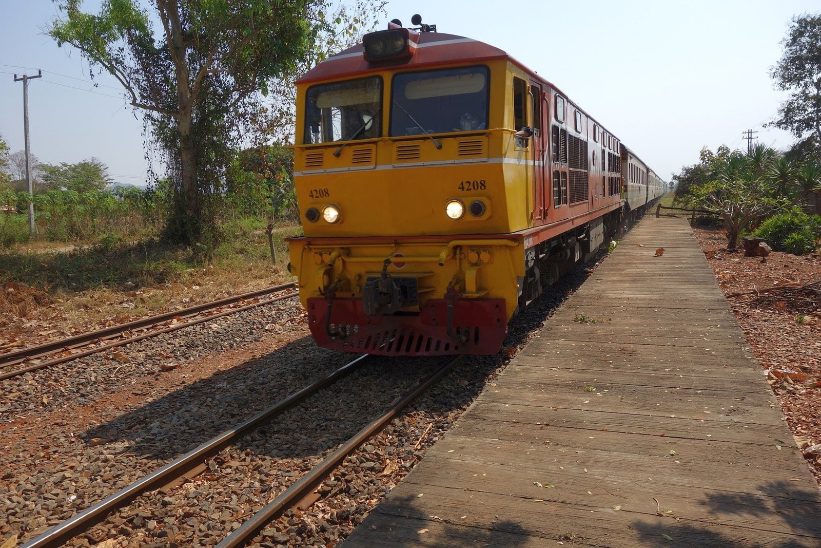Train coloré en Thaïlande sur une voie ferrée rurale.