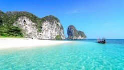 Plage de sable blanc avec eaux turquoise et falaises verdoyantes.