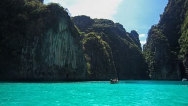 Baie turquoise avec falaises verdoyantes et bateau en mer.