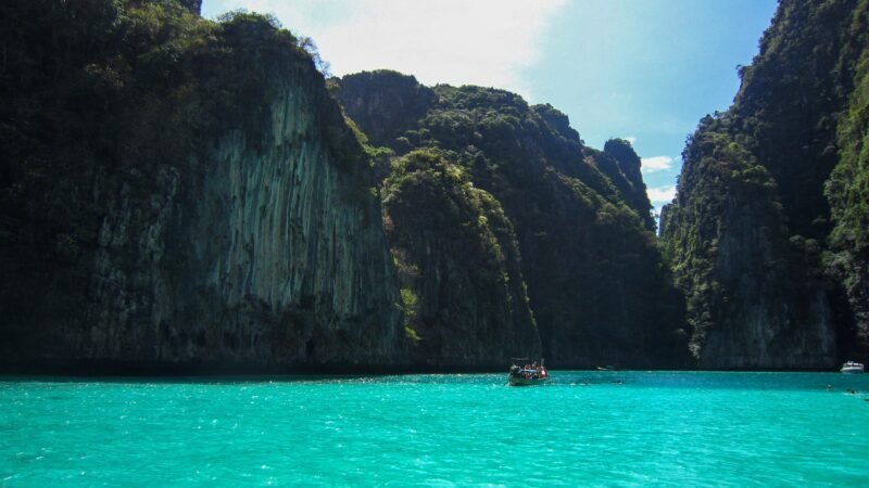Baie turquoise avec falaises verdoyantes et bateau en mer.