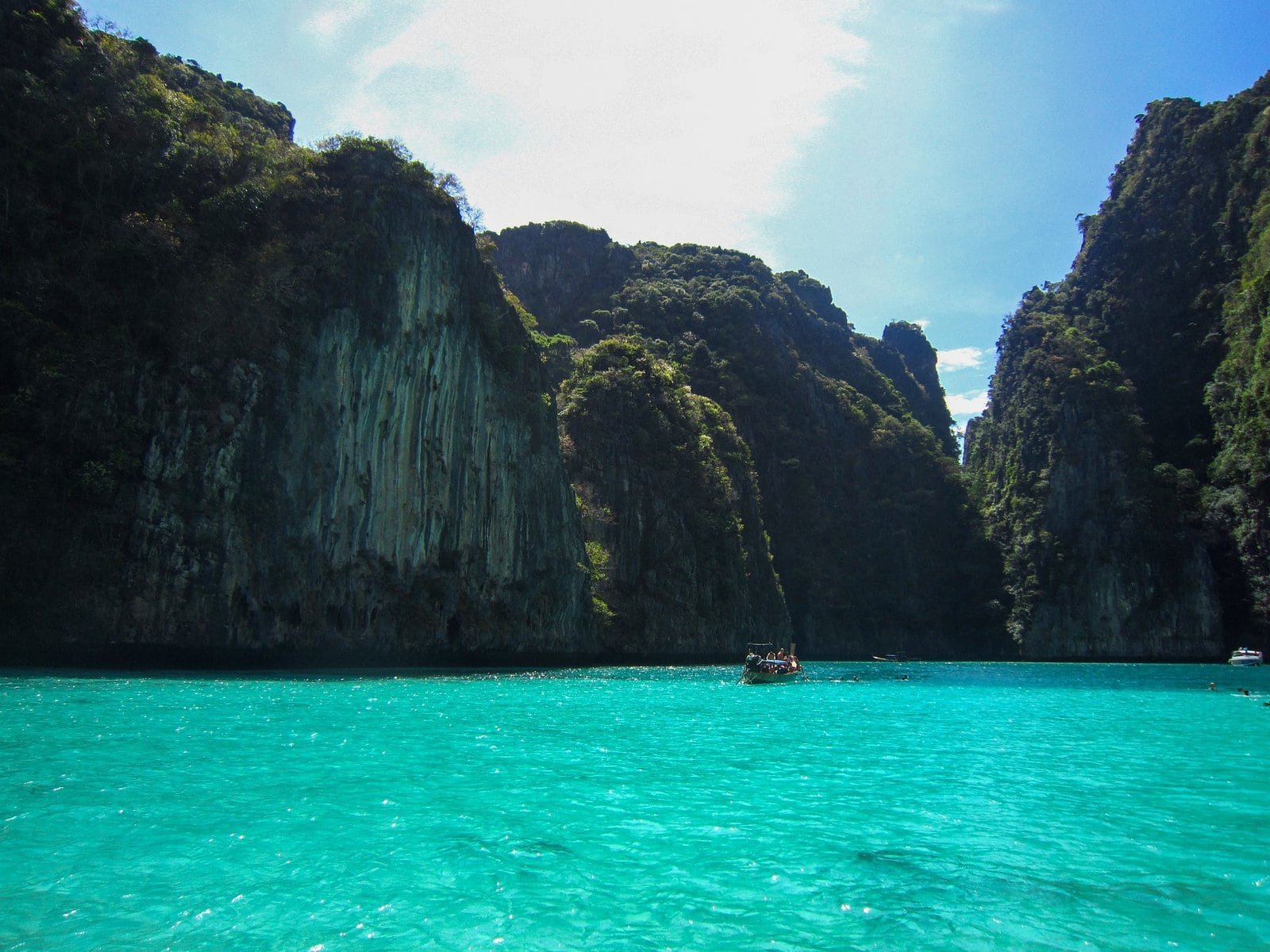 Baie turquoise avec falaises verdoyantes et bateau en mer.