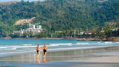 Deux personnes marchent sur la plage en Thaïlande avec vue sur la mer et la montagne.