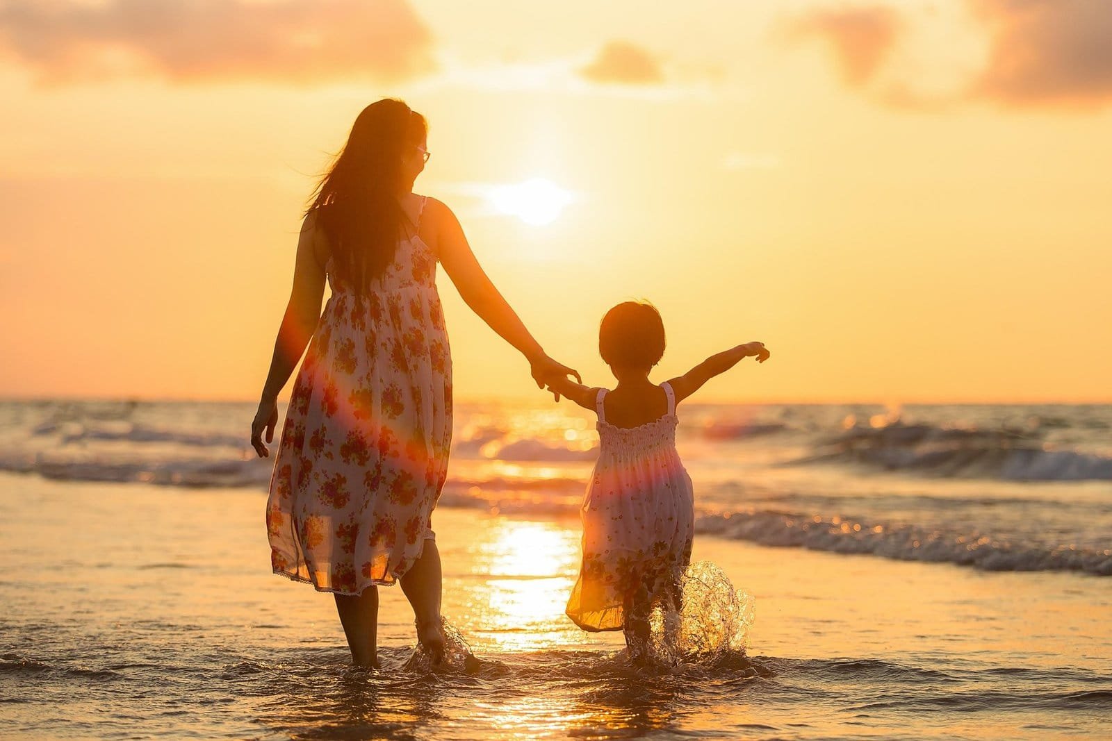 Mère et fille marchant sur la plage au coucher du soleil.