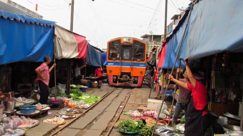 Train traverse le marché de Mae Klong, passant entre les étals colorés.